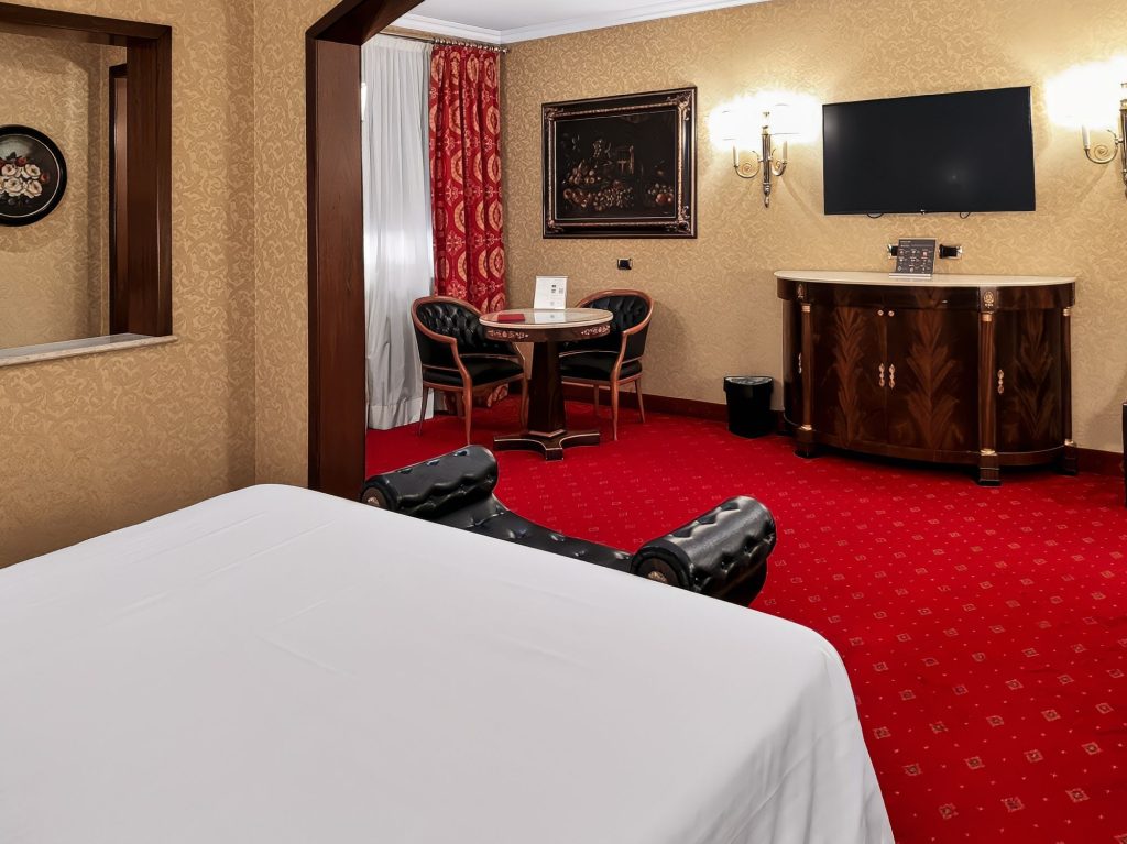 Salottino della Suite Deluxe con tavolino, poltrone, TV e moquette rossa